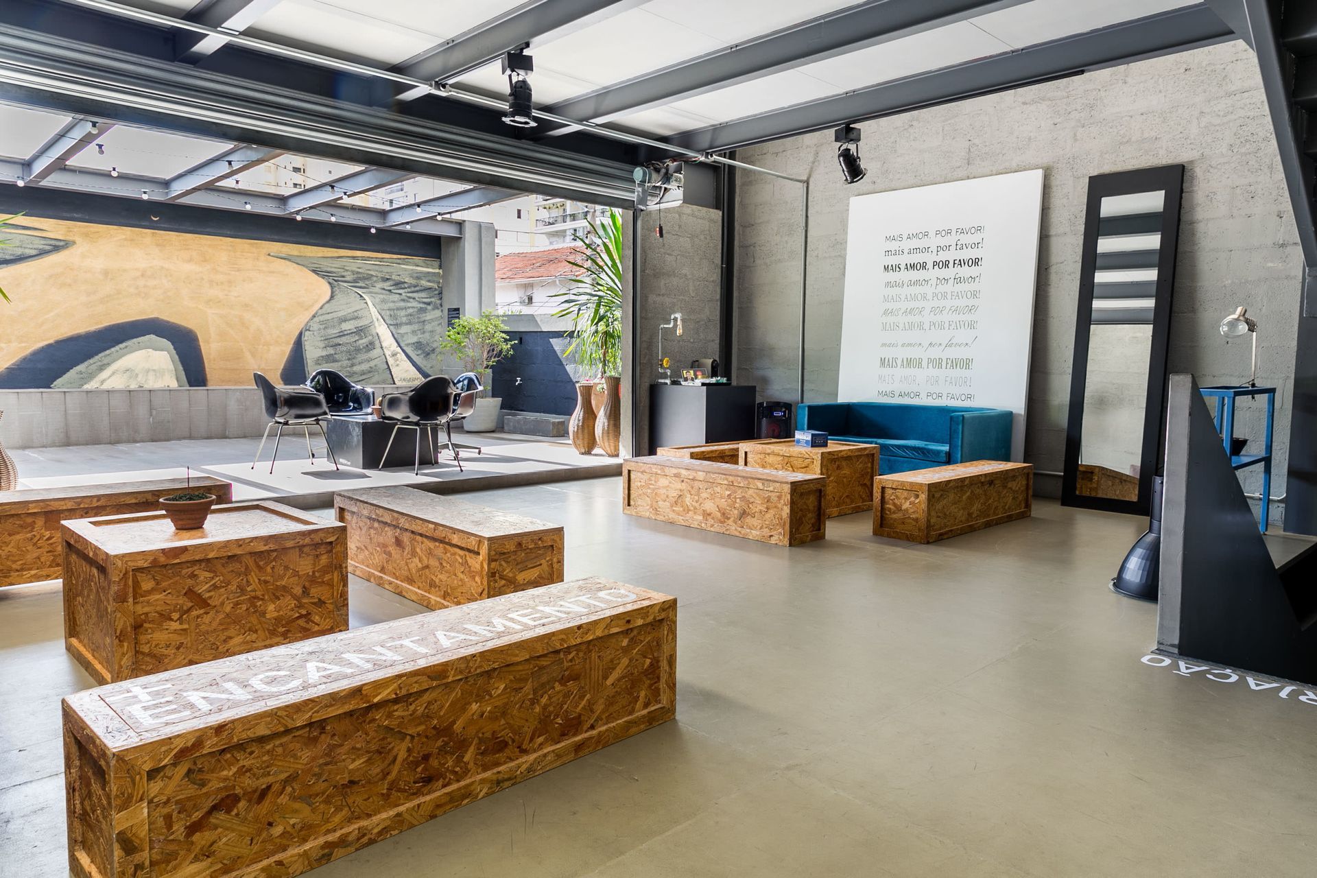 Sala de estar moderna em estilo garagem, com bancos de madeira, pufes e um mural na parede.