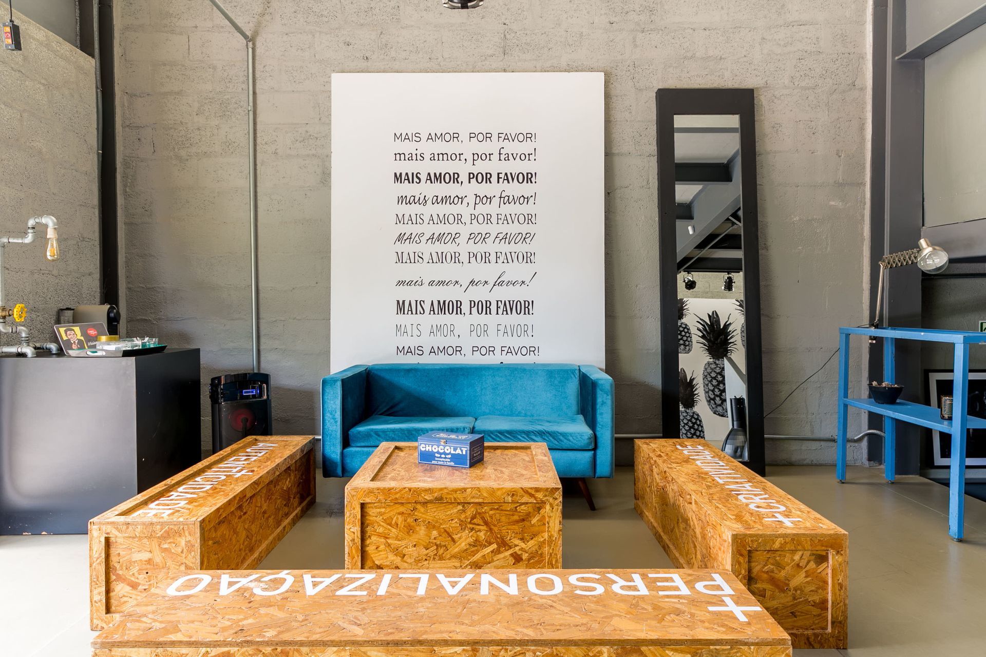 Sala de estar moderna com assentos azuis e laranjas ao redor de uma mesa baixa de madeira em um interior industrial.
