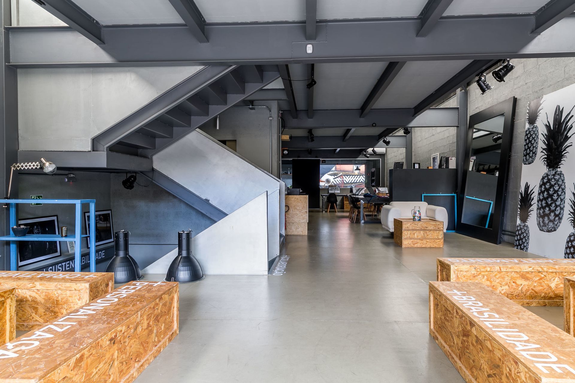 Sala de estar moderna com estilo industrial, com escada, piso de concreto e assentos de vime.