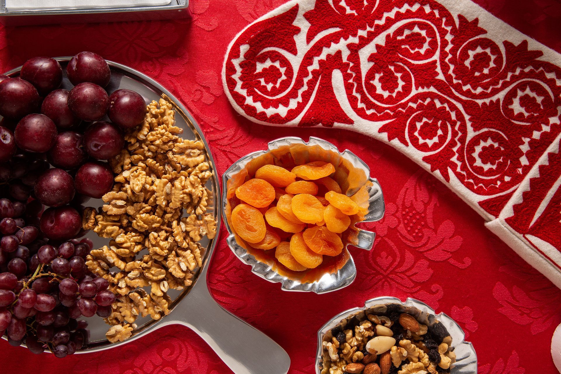 Frutas secas e nozes variadas em pequenas tigelas sobre uma toalha de mesa vermelha estampada.