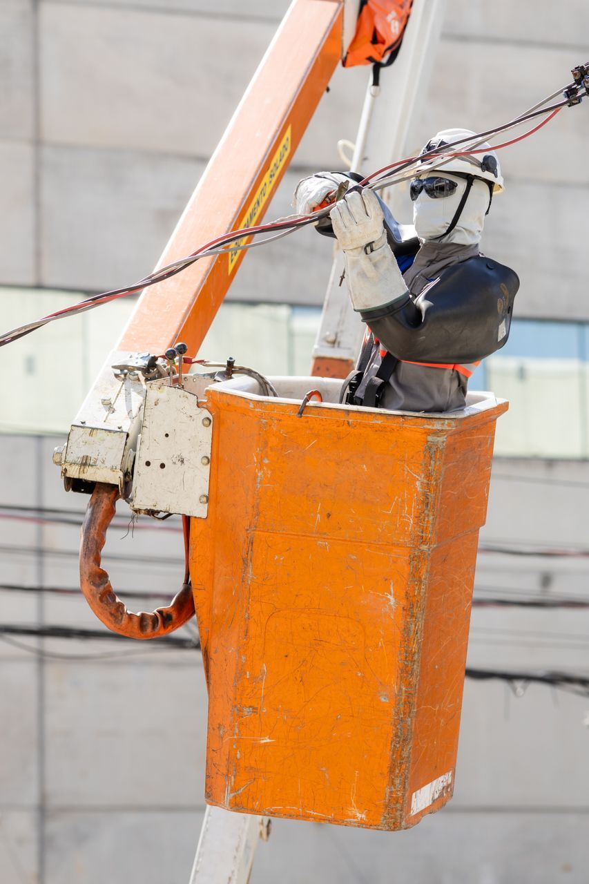 Plataforma elevatória laranja com equipamentos elétricos e cabos ao fundo, em um prédio.