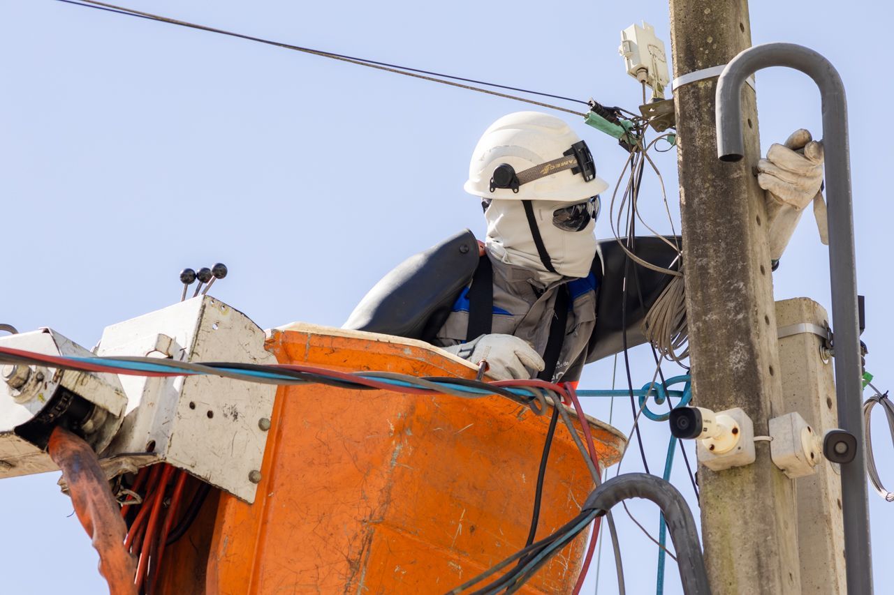 Operário de serviços públicos em uma plataforma elevatória laranja reparando linhas de energia em um poste.