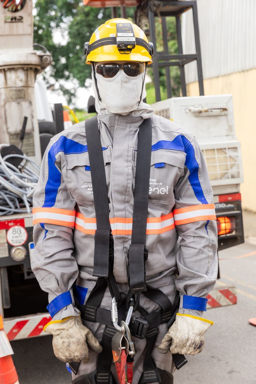 Operário da construção civil com equipamento de segurança cinza, capacete, óculos de proteção e máscara facial, em pé em um canteiro de obras.
