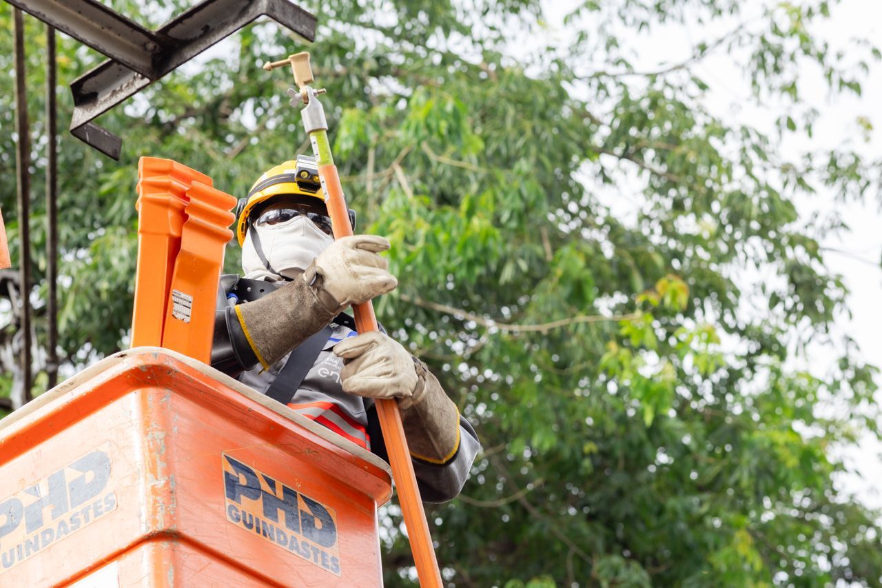 Operário com equipamento de segurança limpando a fachada de um prédio a partir de uma plataforma elevatória laranja.