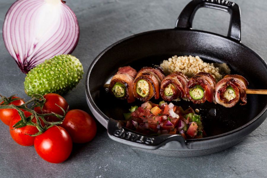 Frigideira com rolinhos de cebola recheados e legumes picados, acompanhados de cebola roxa inteira, brócolis e tomates.