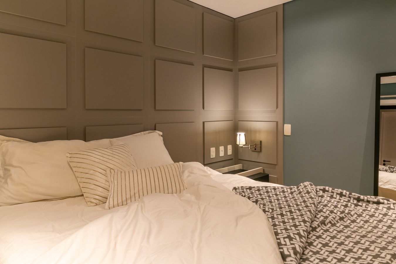 Quarto aconchegante com uma grande cama branca, paredes com painéis bege e iluminação suave e quente.