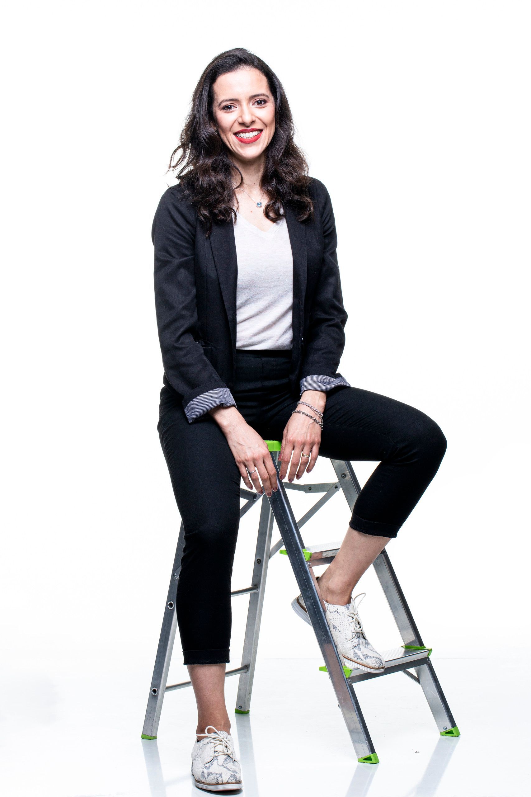 Mulher sentada em uma escada, sorrindo, contra um fundo branco.