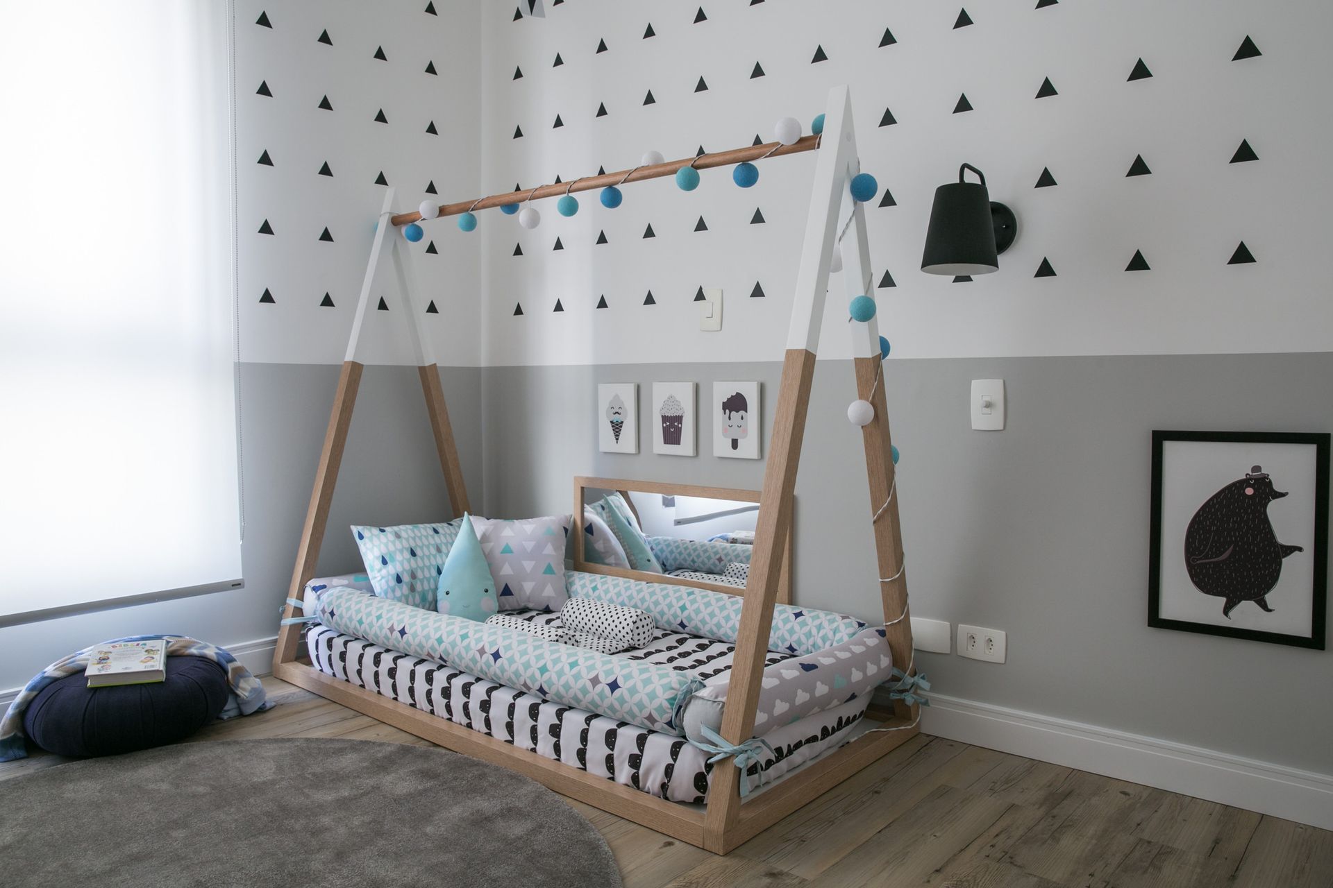 Cama infantil com dossel e roupa de cama estampada em um quarto de bebê cinza com adesivos de parede triangulares.