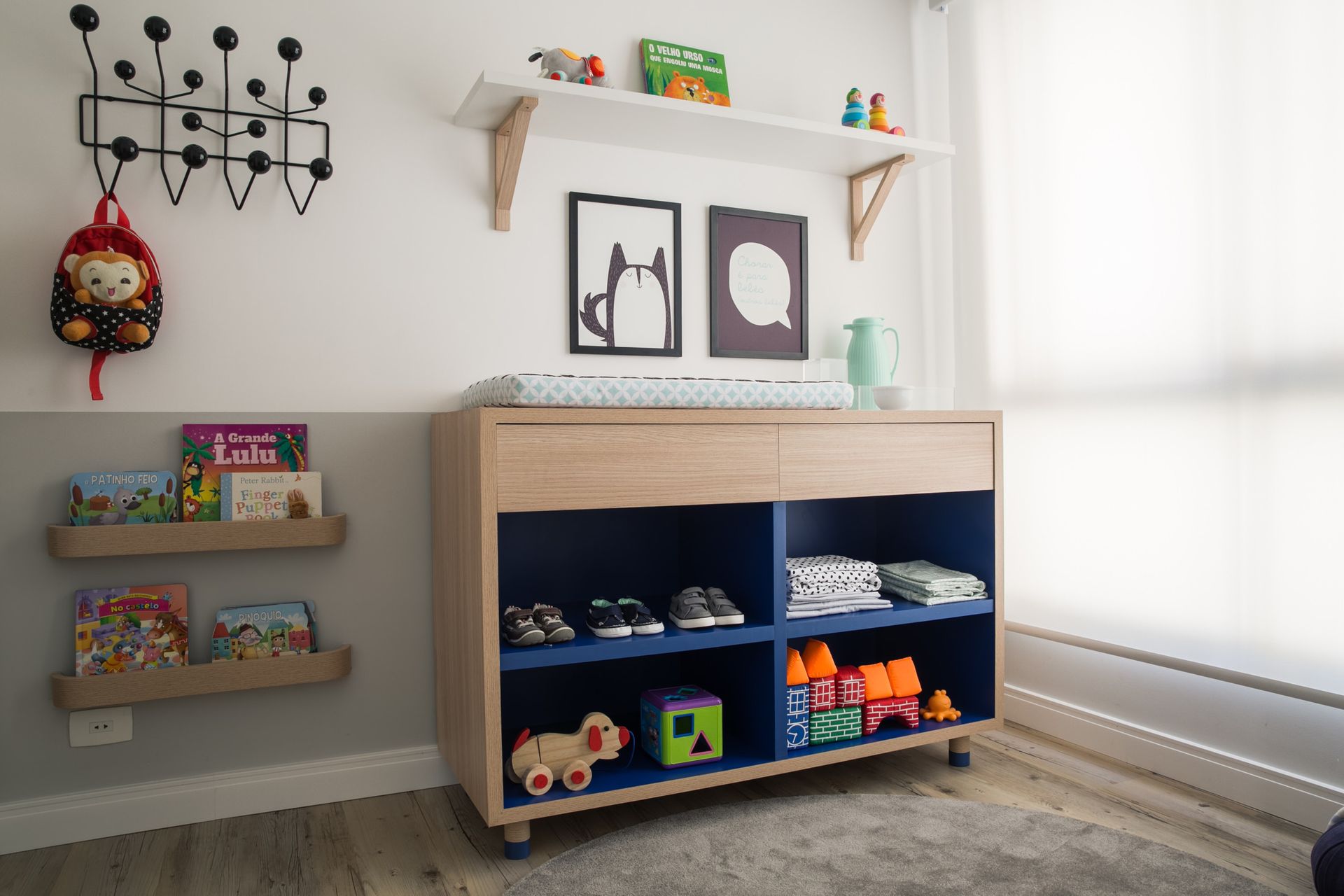 Cantinho de brincar infantil com prateleiras para guardar brinquedos, livros, quadros e uma grande janela.