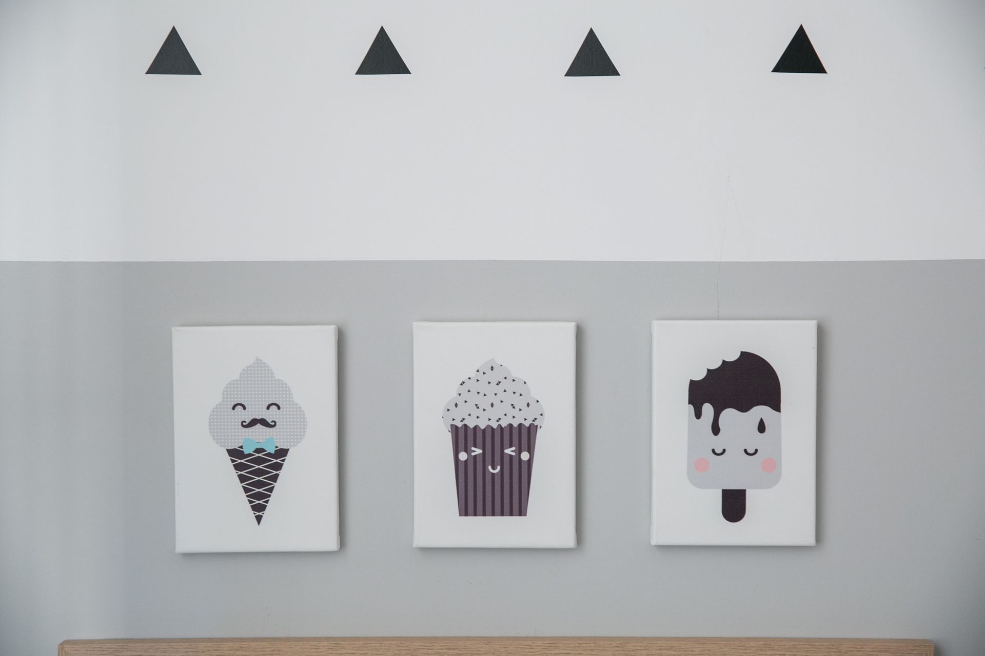 Três gravuras de sorvete e cupcake em uma parede cinza com pequenos adesivos triangulares pretos acima.