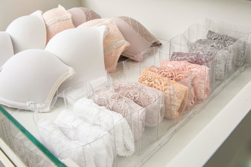 Sutiãs coloridos e peças de lingerie de renda dispostos em caixas transparentes sobre uma prateleira branca.