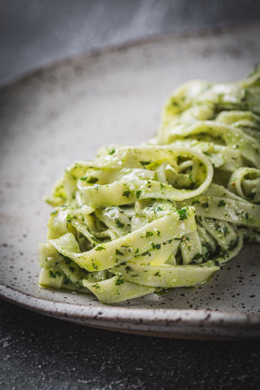 Massa fettuccine ao molho cremoso de ervas verdes servida em um prato cinza com pintas.