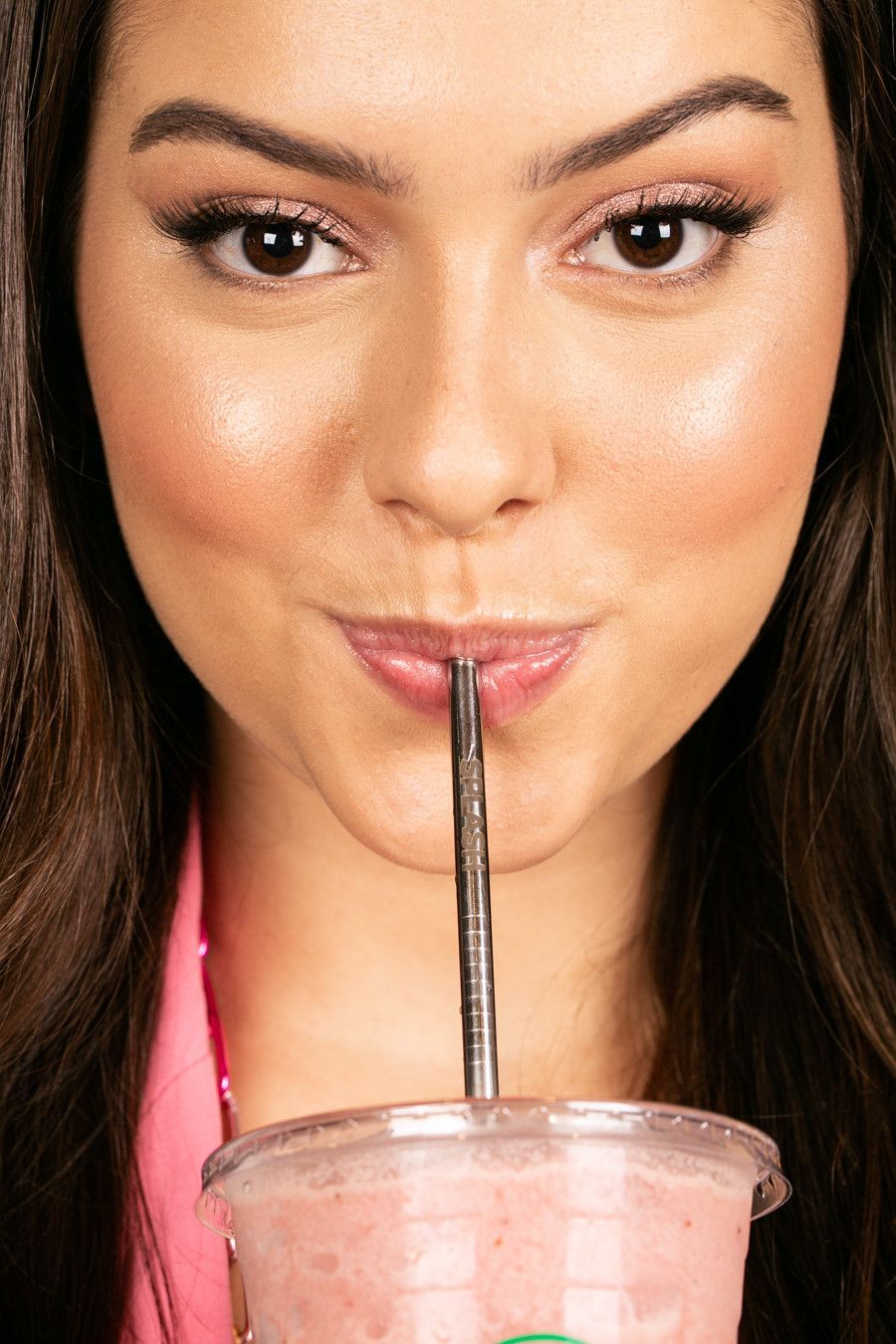 Mulher tomando um drinque rosa com canudo, close-up com expressão neutra.