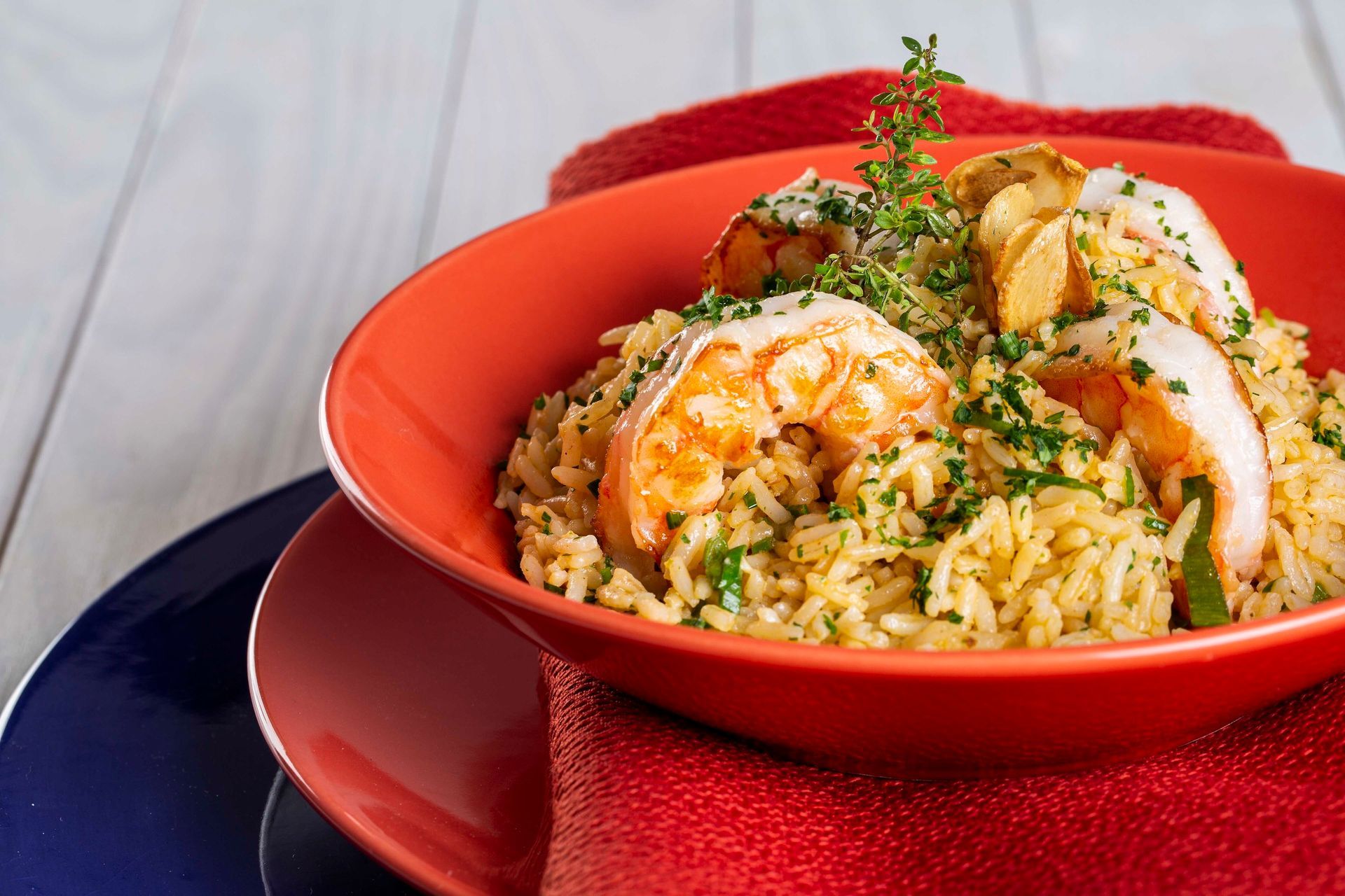 Tigela vermelha de arroz com salmão e molho em um prato escuro, decorada com ervas.