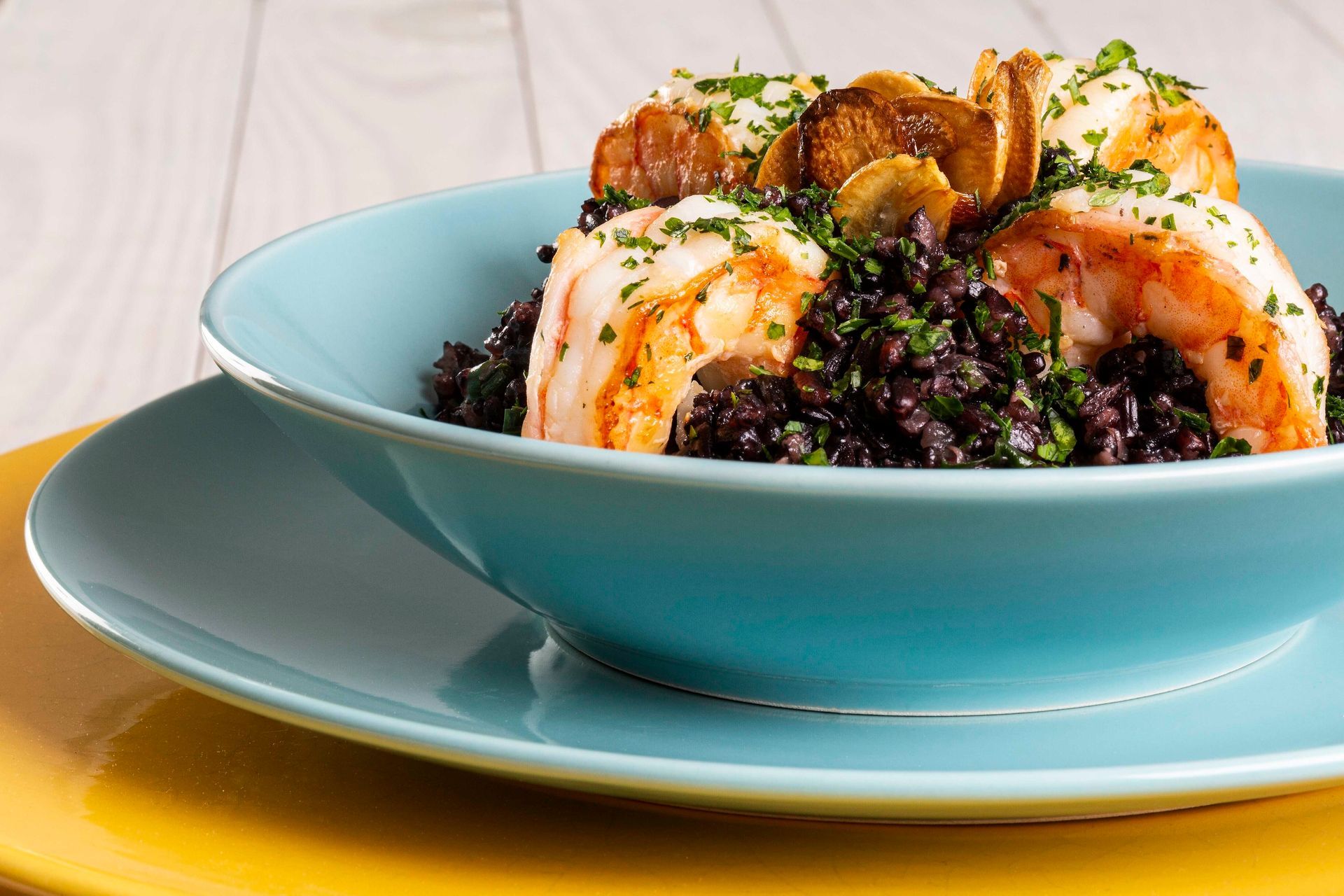 Prato de camarão com arroz preto em uma tigela turquesa sobre um prato combinando.
