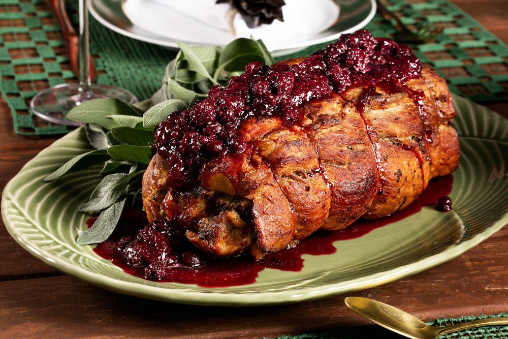 Carne assada coberta com molho de cranberry em uma travessa verde em uma mesa de festa.