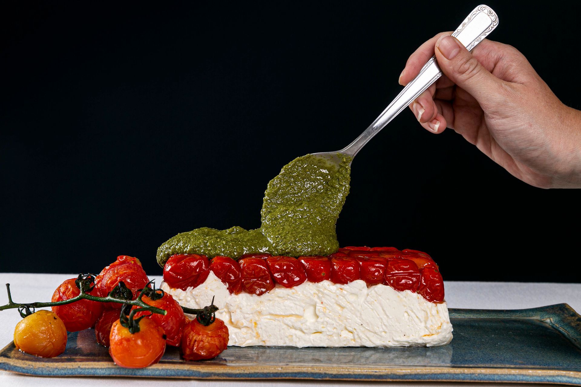 Mão colocando molho verde sobre a sobremesa em camadas, coberta com frutas vermelhas e frutas vermelhas, em um prato de servir.