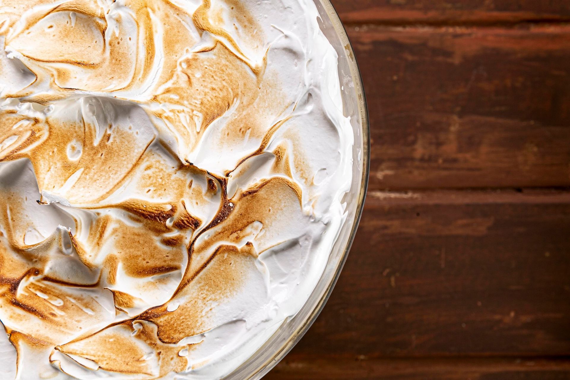 Sobremesa de merengue tostado em um prato branco sobre uma mesa de madeira.