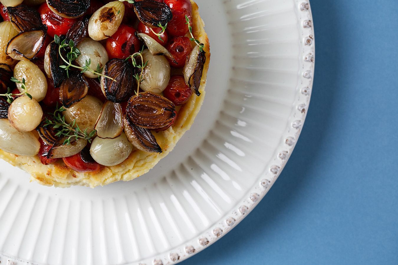 Detalhe de uma torta de legumes com tomates e cogumelos em um prato branco sobre um fundo azul.