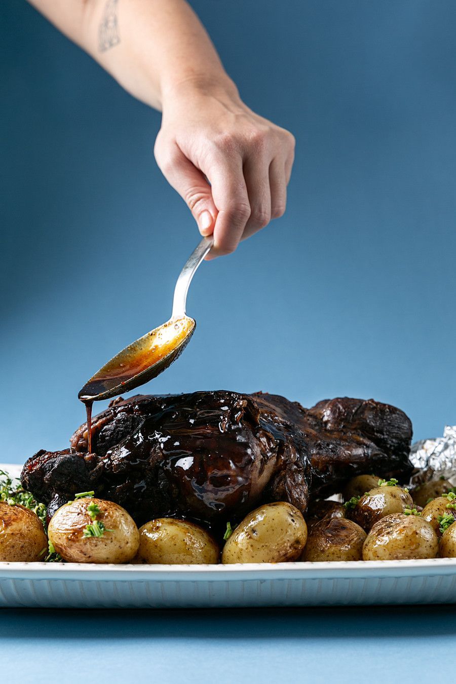 Molho sendo despejado à mão sobre carne assada e batatas em um prato azul.