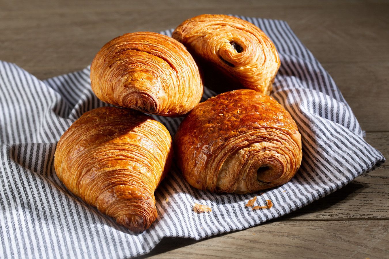 Quatro croissants dourados sobre uma toalha listrada em cima de uma mesa de madeira.