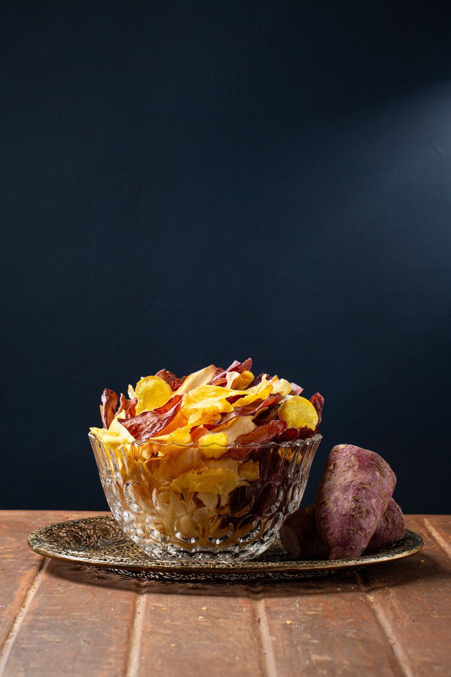 Sobremesa em uma tigela de vidro sobre uma mesa de madeira, decorada com fatias de laranja, ao lado de um cristal roxo sobre um fundo escuro.