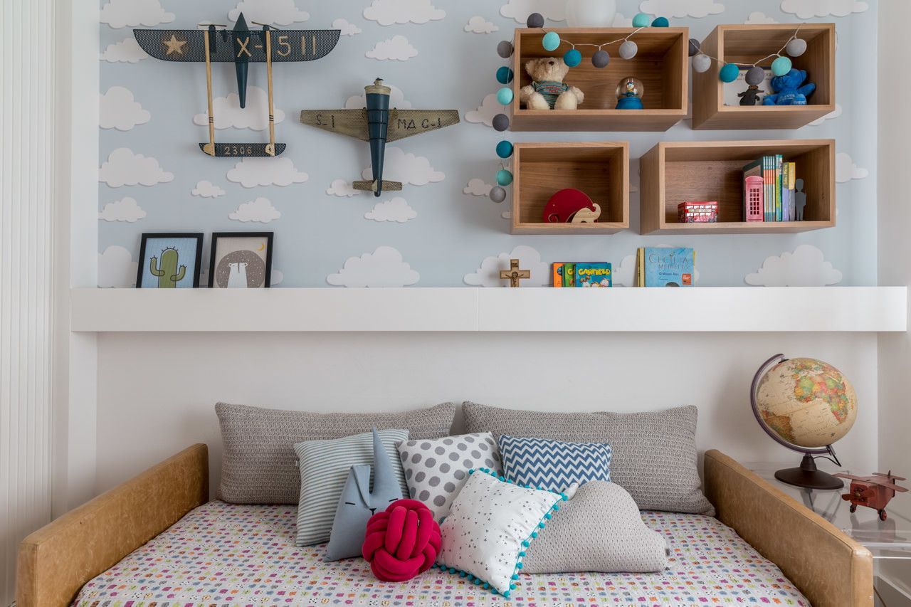 Quarto infantil com cama baixa, roupa de cama estampada, prateleiras na parede, livros e um globo terrestre.