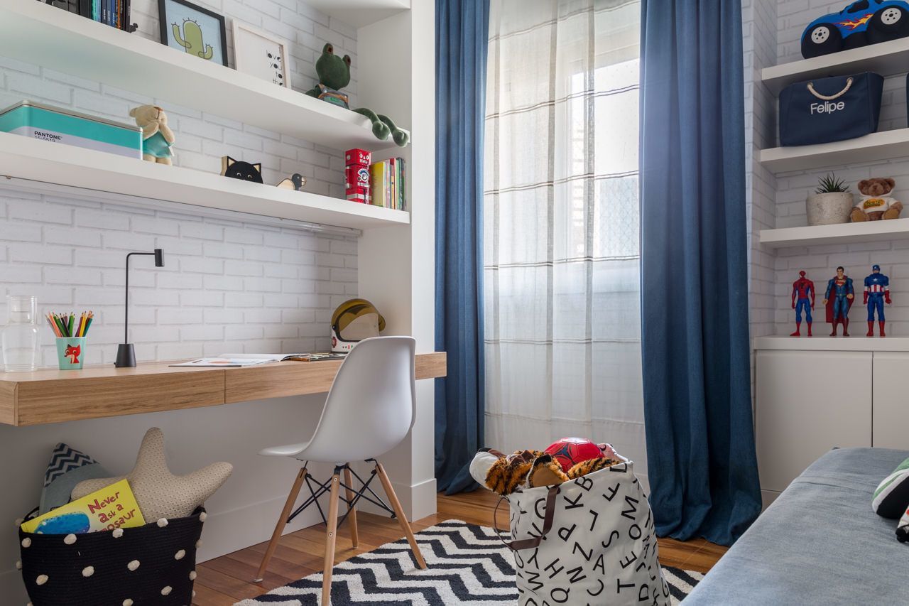 Quarto infantil iluminado com escrivaninha branca, cortinas azuis, prateleiras e tapete preto e branco.