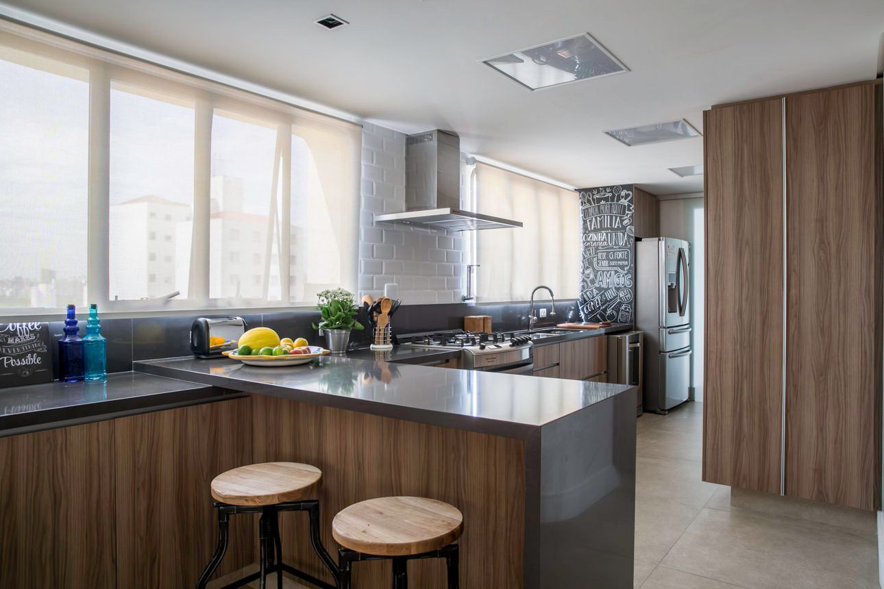 Cozinha moderna com armários de madeira, janelas amplas, ilha e banquetas.