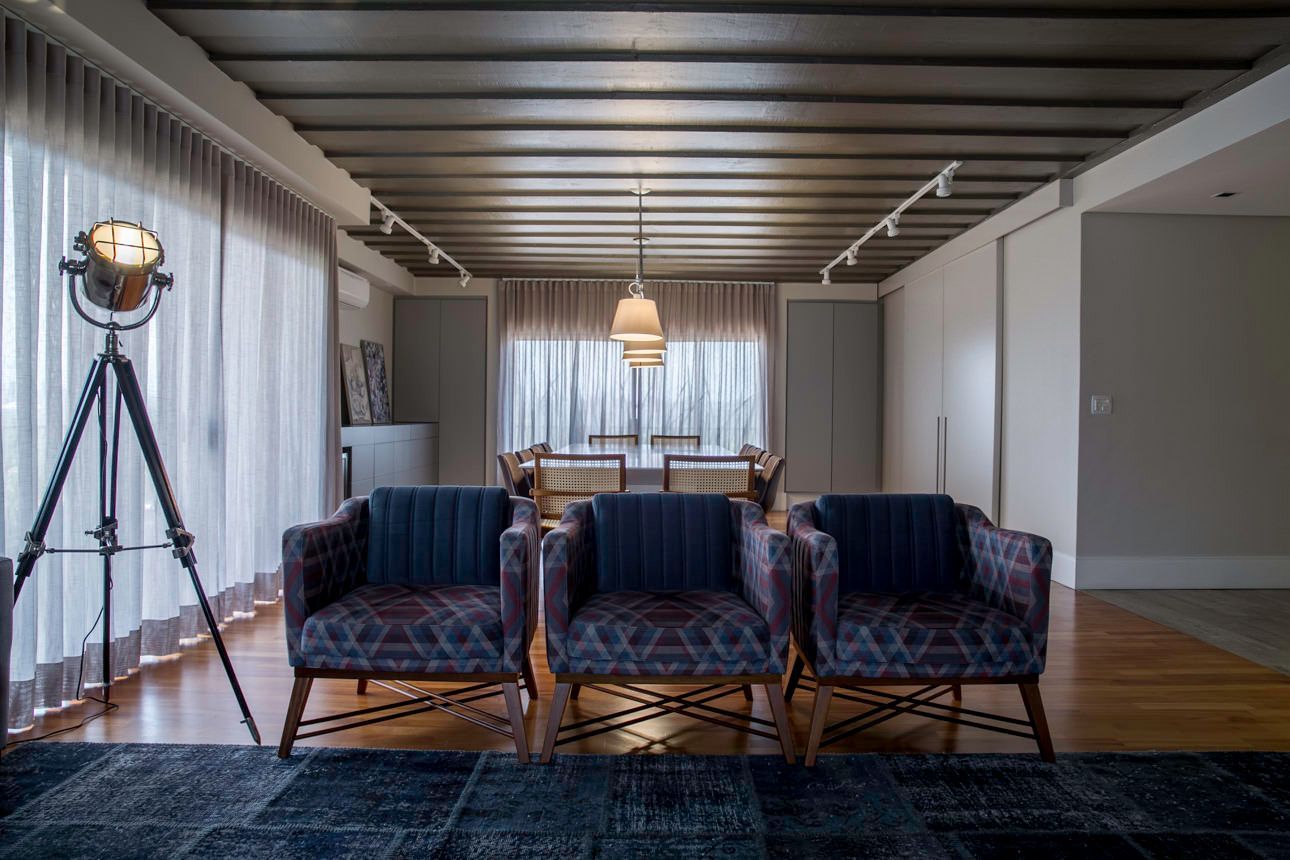 Sala de estar moderna com cadeiras de veludo azul, papel de parede listrado e um abajur de tripé junto à janela.