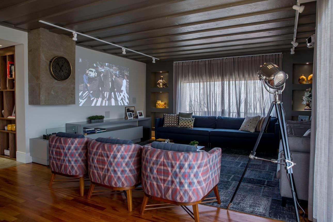 Sala de estar moderna com sofá, três cadeiras estampadas, tela de projeção e luminária de tripé.