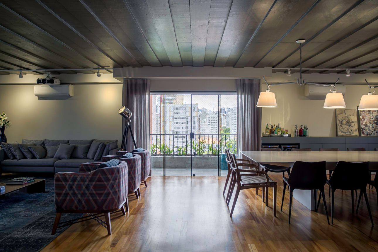 Sala de estar e jantar moderna em plano aberto com sofá, piso de madeira, luminárias pendentes e portas de varanda com vista para os edifícios da cidade.