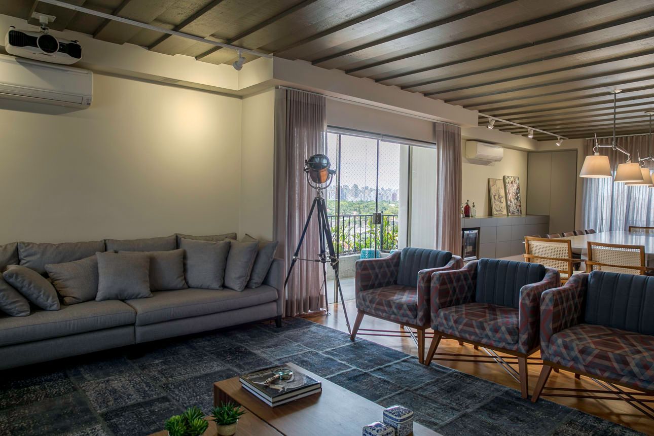 Sala de estar moderna com sofá cinza, cadeiras xadrez, mesa de centro e janelas amplas com cortinas translúcidas.