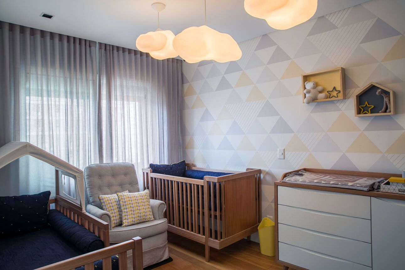 Quarto de bebê com berço, poltrona, cômoda trocadora e papel de parede estampado sob luzes suaves em formato de nuvem.
