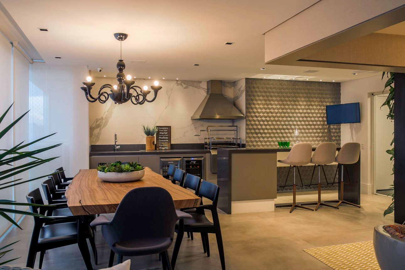 Cozinha e sala de jantar modernas em conceito aberto, com mesa de madeira, lustre, banquetas e backsplash de azulejos.