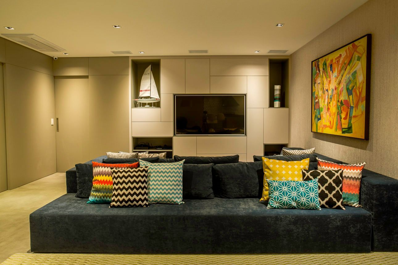 Sala de estar moderna com sofá escuro, almofadas coloridas, TV fixada na parede e obras de arte abstratas.