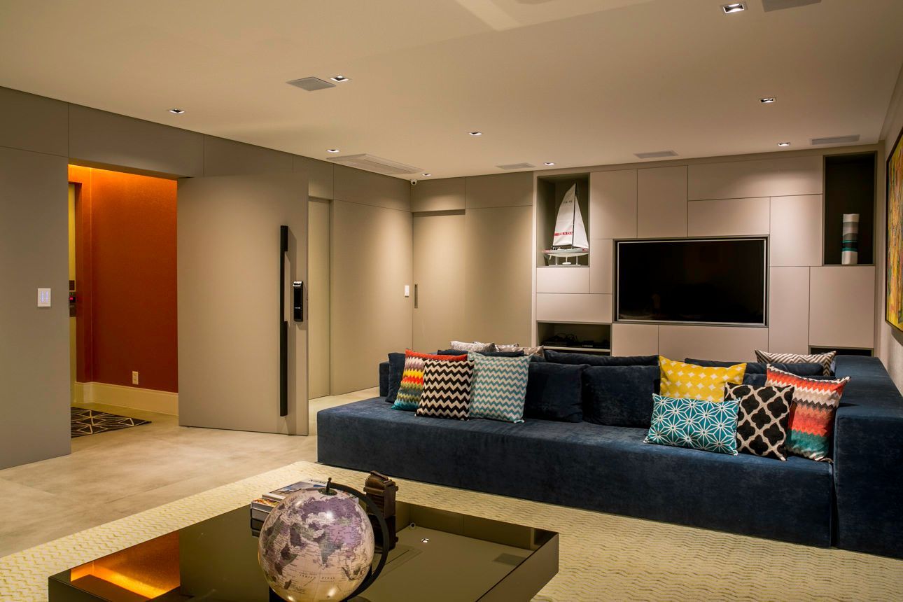 Sala de estar moderna com sofá azul, almofadas coloridas, TV fixada na parede e iluminação embutida aconchegante.