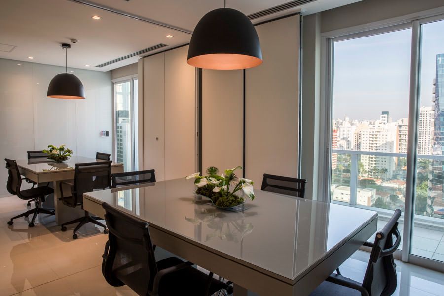 Sala de reuniões moderna com mesa de vidro, cadeiras pretas, luminárias pendentes e vista para a cidade através de grandes janelas.