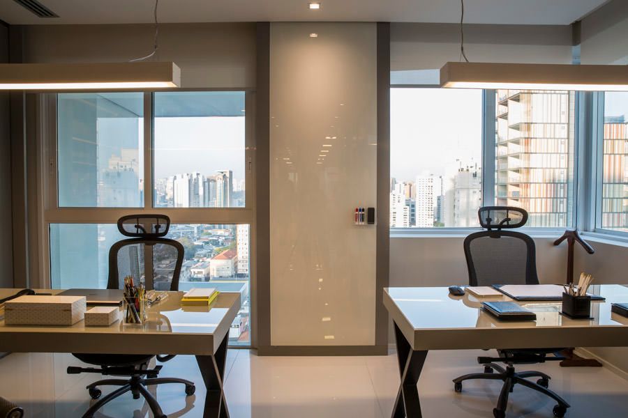 Espaço de trabalho moderno com duas mesas, cadeiras ergonômicas e amplas janelas com vista para a cidade.