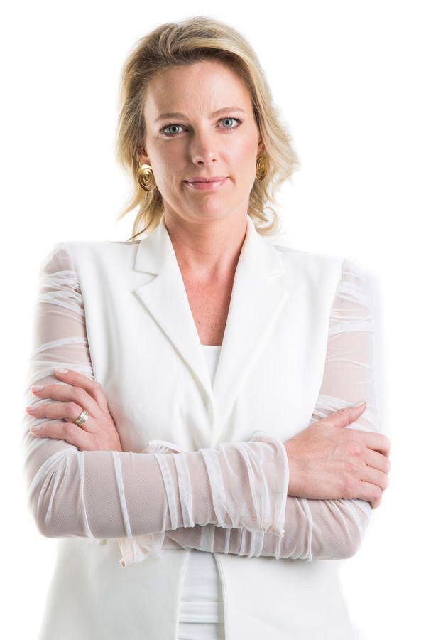 Mulher de blazer branco em pé com os braços cruzados contra um fundo branco