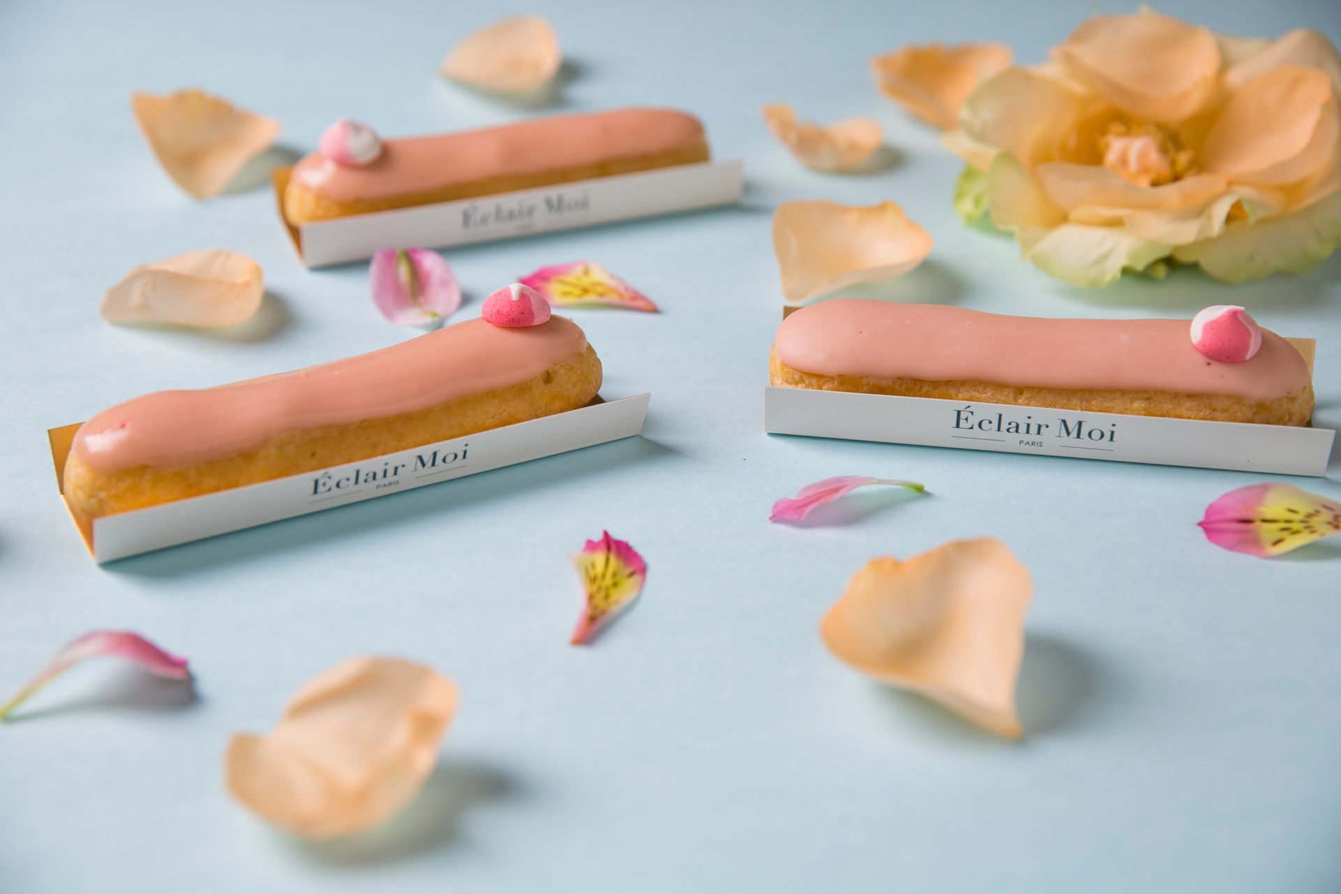 Barrinhas de sobremesa em tons pastel de rosa e dourado com pétalas de rosa sobre um fundo azul claro.