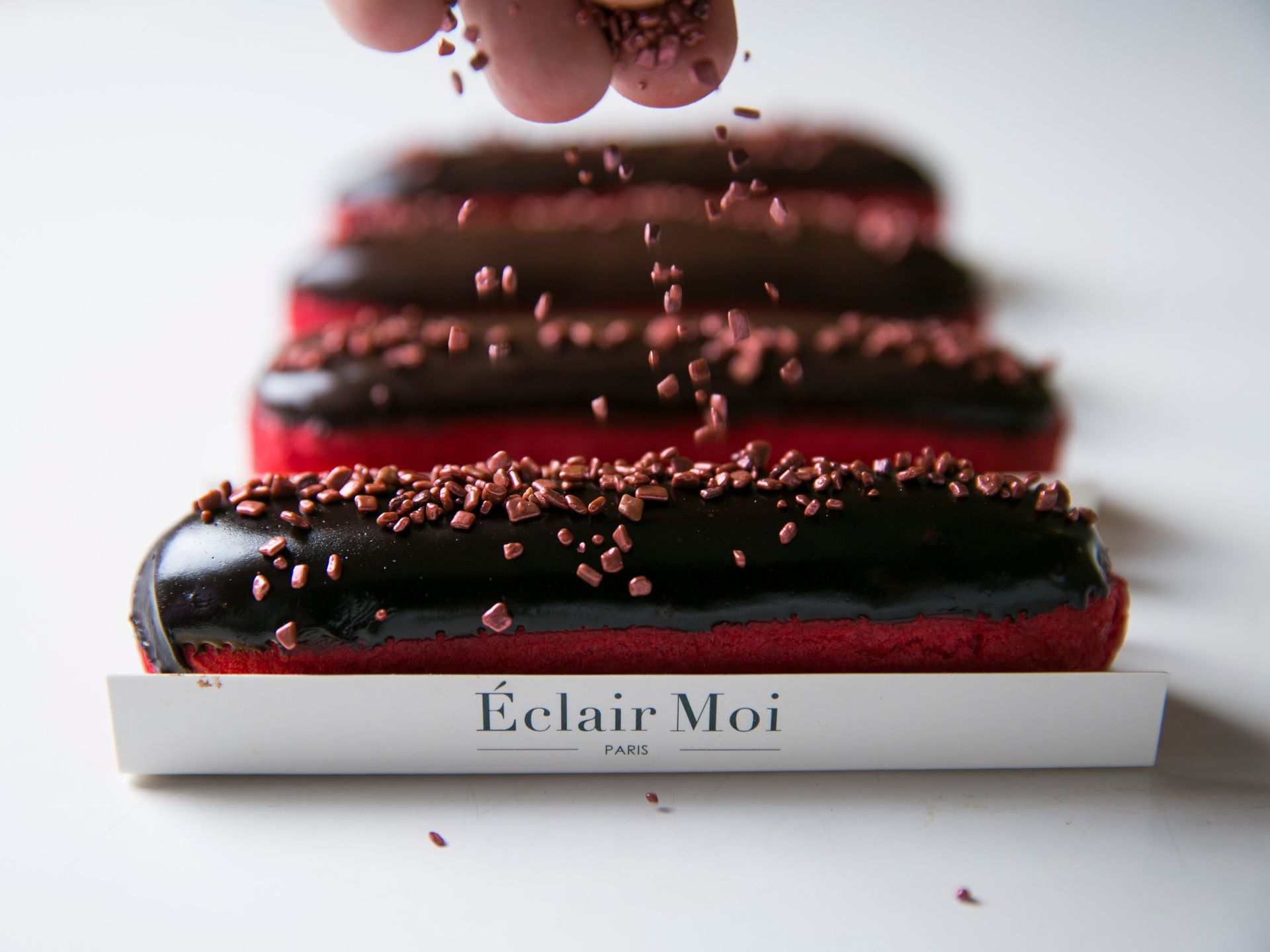 Éclairs com cobertura de chocolate empilhados em uma bandeja branca com açúcar de confeiteiro ou cacau em pó por cima.
