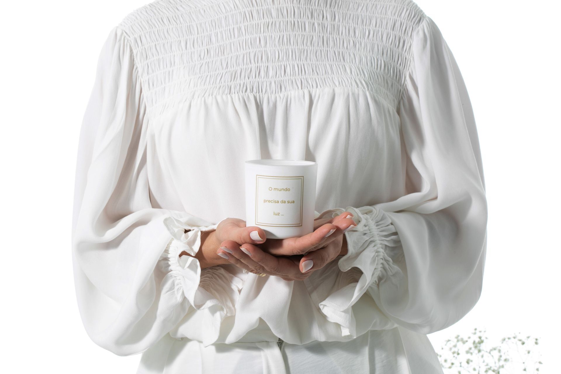 Pessoa de blusa branca segurando um castiçal com as duas mãos.