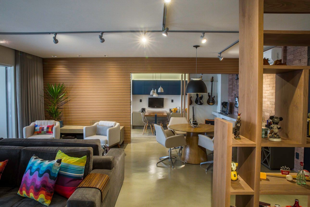 Sala de estar moderna com parede de destaque em madeira, sofá, mesa de jantar e almofadas coloridas em primeiro plano.
