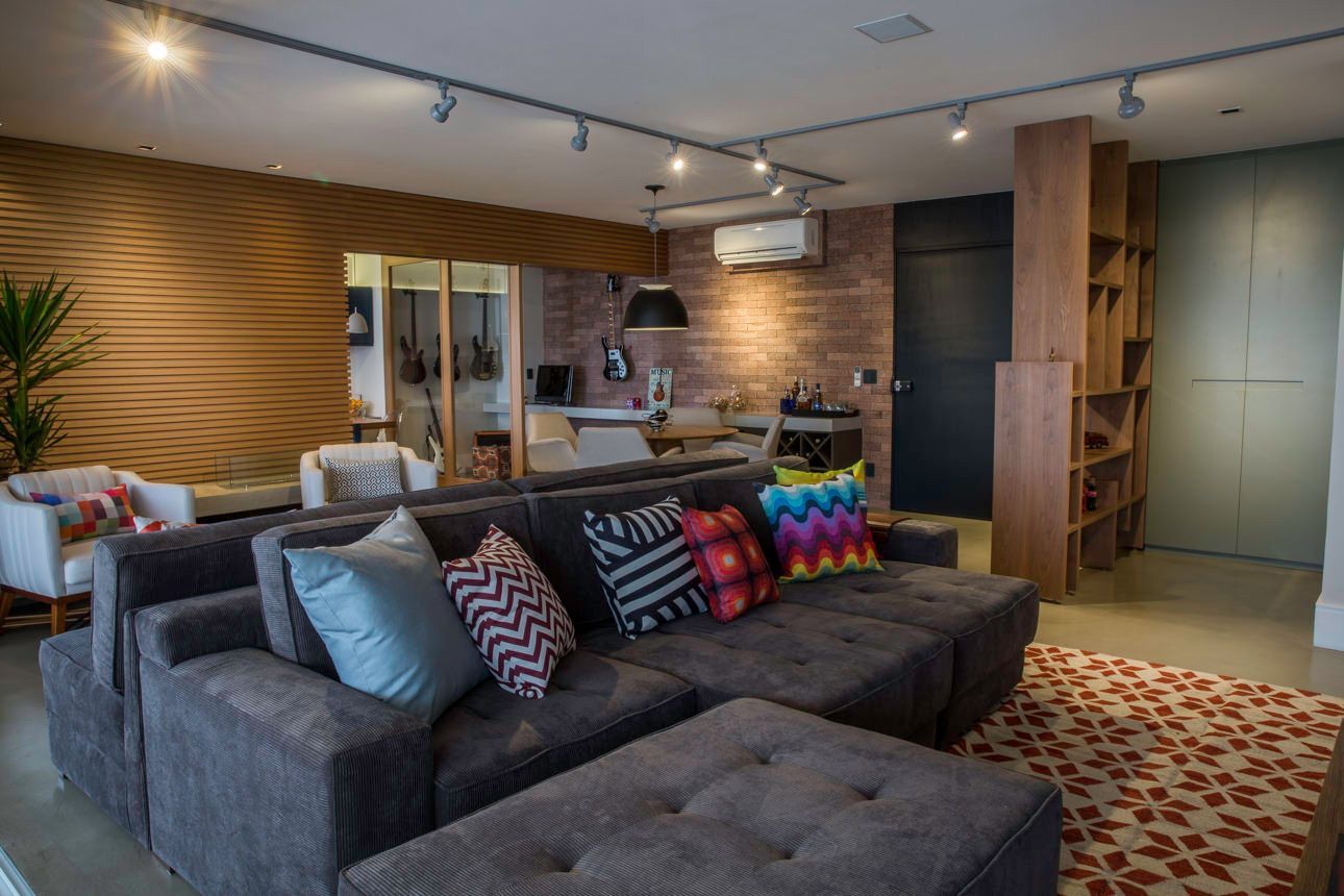 Sala de estar moderna com sofá modular cinza, almofadas coloridas e parede com painéis de madeira.