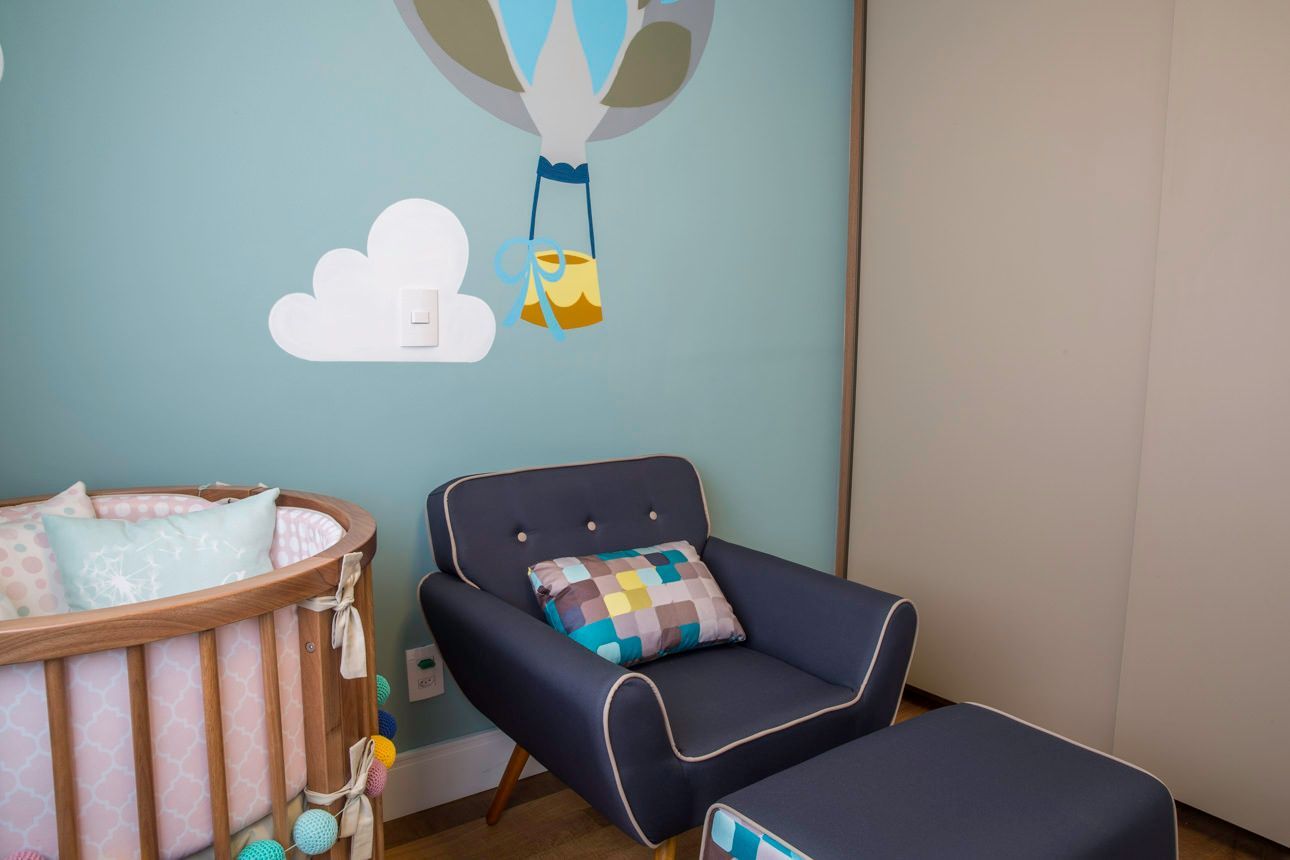 Cantinho do quarto do bebê com cadeira azul-marinho, berço, pufe e adesivo de parede de balão de ar quente.