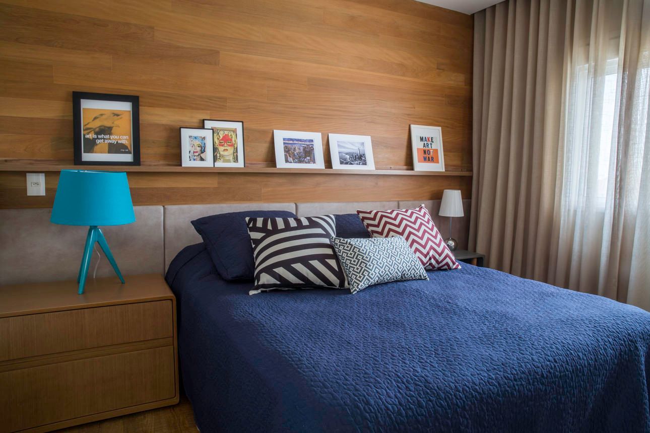 Quarto aconchegante com colcha azul, abajur verde-água, parede de madeira e fotos emolduradas em uma prateleira.