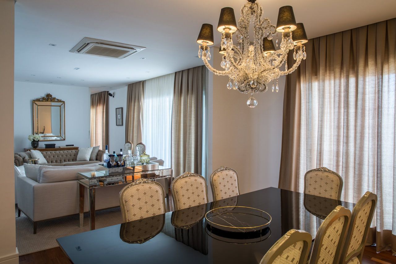 Sala de jantar e estar elegante com lustre de cristal, mesa preta, cadeiras bege e grandes janelas com cortinas.