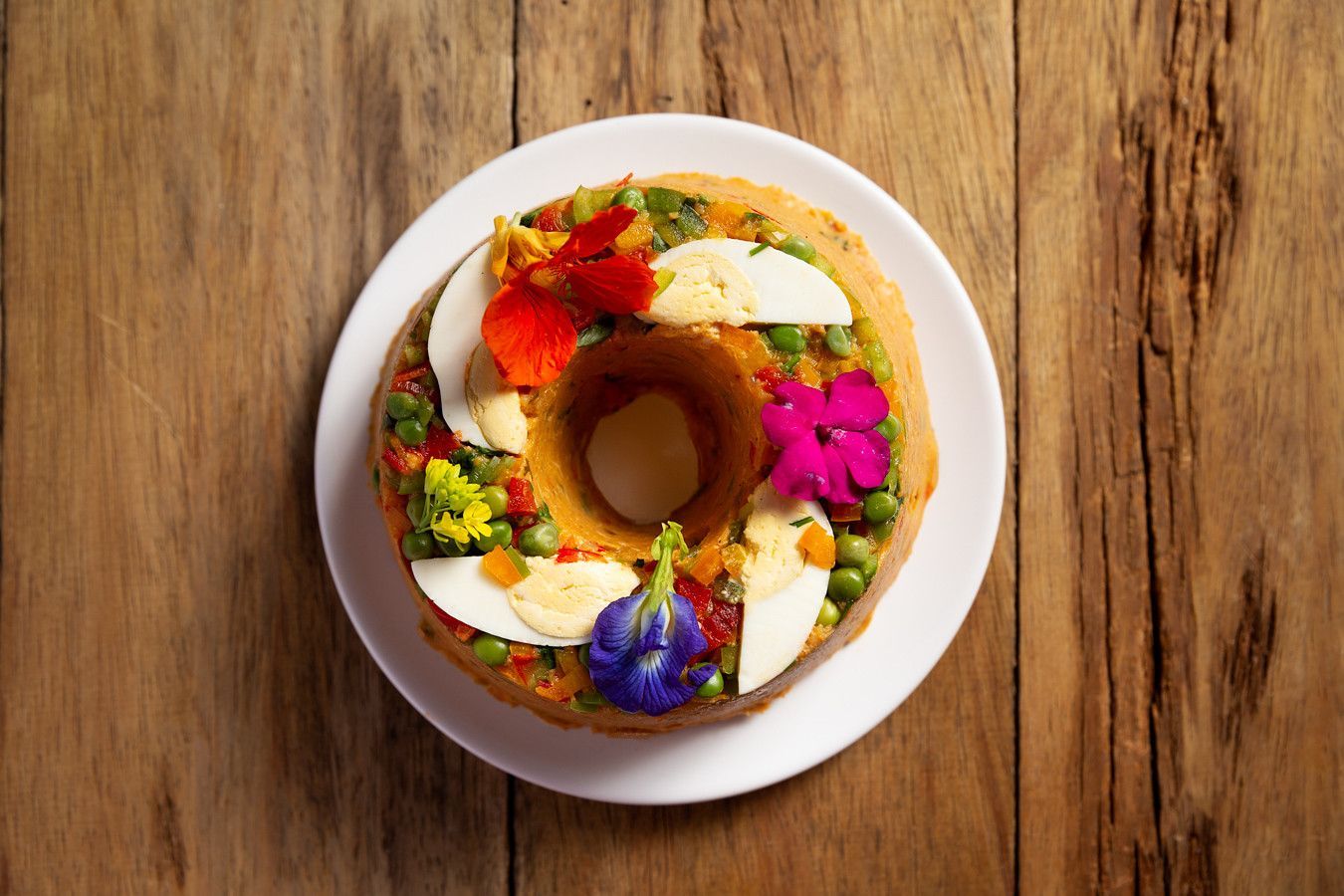 Rosquinhas coloridas sortidas em um prato branco sobre uma mesa de madeira.