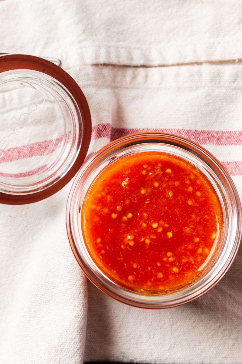 Abra um frasco de molho de pimenta vermelho vivo sobre um pano branco com listras rosa.